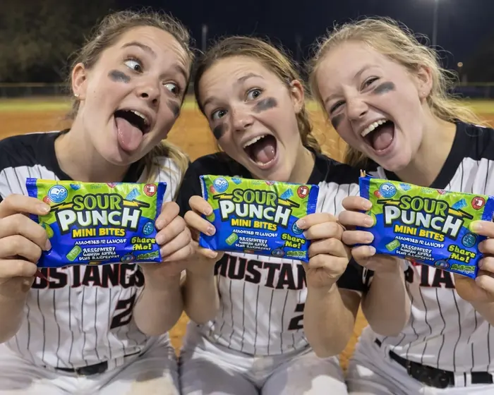 Three college student Brand Advocates in athletic uniforms holding consumer snack products at an EvolveZ campus program